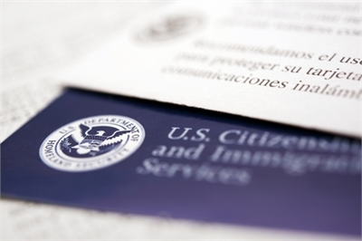 [ai] A close-up view of a U.S. Citizenship and Immigration Services card showing the official seal and text, partially obscured by a white document with text in Spanish.